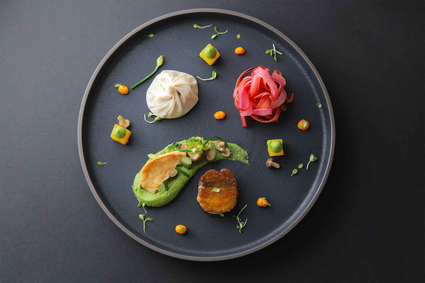 Gourmet dish with dumpling, pickled vegetables, and seared protein on plate.